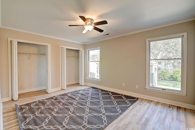 unfurnished bedroom with multiple closets, crown molding, multiple windows, and hardwood / wood-style flooring