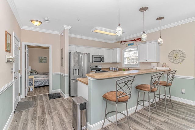 kitchen featuring a breakfast bar, white cabinetry, hanging light fixtures, stainless steel appliances, and kitchen peninsula