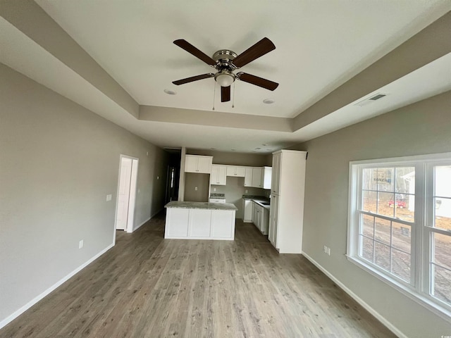 kitchen featuring a tray ceiling, light wood-style flooring, baseboards, and visible vents