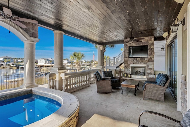 view of patio with ceiling fan, a water view, and an outdoor stone fireplace