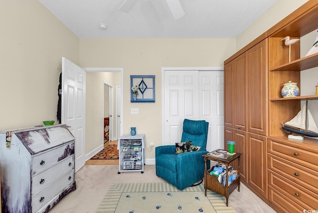 living area with ceiling fan, baseboards, a textured ceiling, and light colored carpet