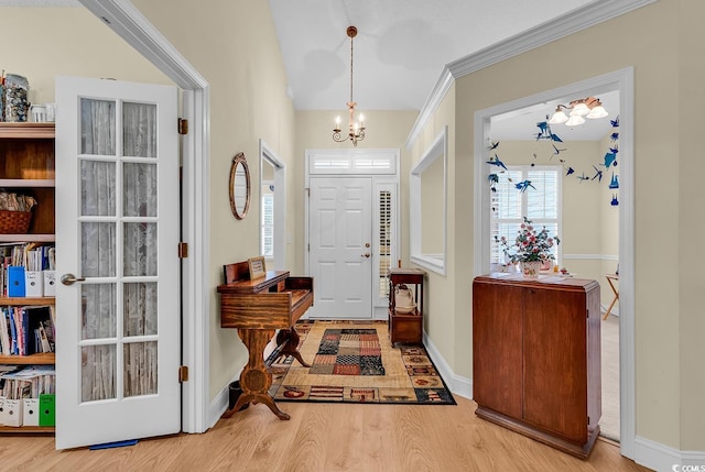 foyer with ornamental molding, light wood-style flooring, baseboards, and an inviting chandelier