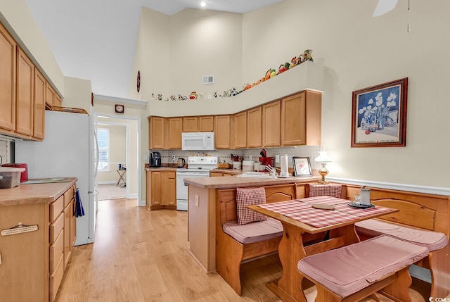 kitchen featuring light countertops, white appliances, high vaulted ceiling, and light brown cabinetry