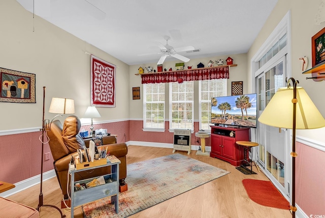 living area with wood finished floors, visible vents, a ceiling fan, wainscoting, and heating unit