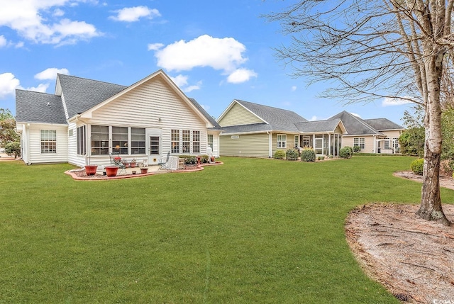 back of property with a patio area, a sunroom, roof with shingles, and a yard