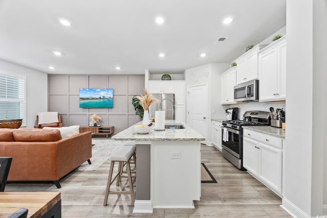 kitchen featuring appliances with stainless steel finishes, a kitchen island with sink, a breakfast bar area, and light stone counters