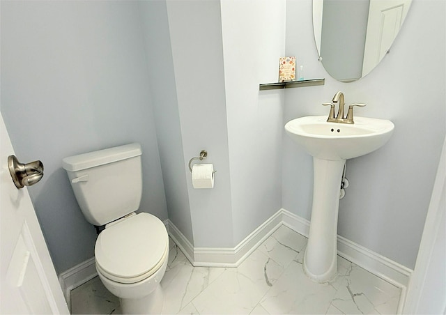 half bathroom featuring toilet, baseboards, a sink, and marble finish floor