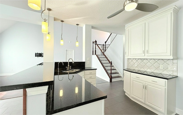 kitchen featuring a peninsula, a sink, white cabinetry, ceiling fan, and decorative backsplash