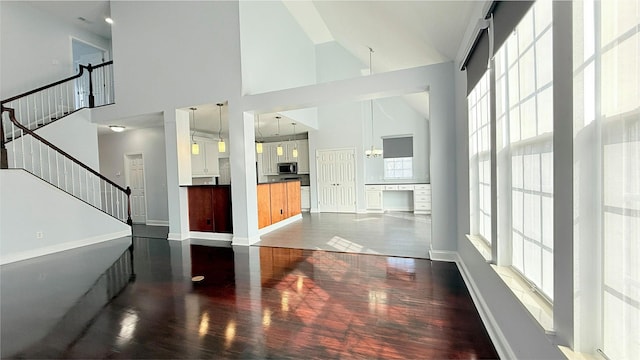 unfurnished living room featuring stairs, a wealth of natural light, high vaulted ceiling, and wood finished floors