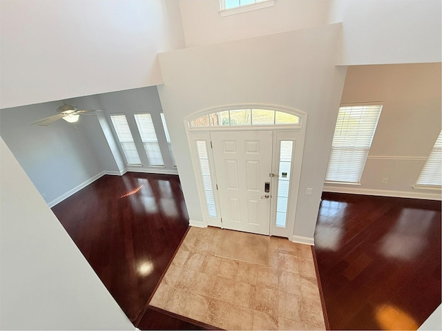 foyer with ceiling fan, a towering ceiling, and light wood-type flooring