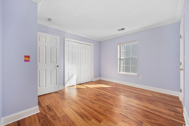 unfurnished bedroom with crown molding, a textured ceiling, a closet, and light wood-type flooring