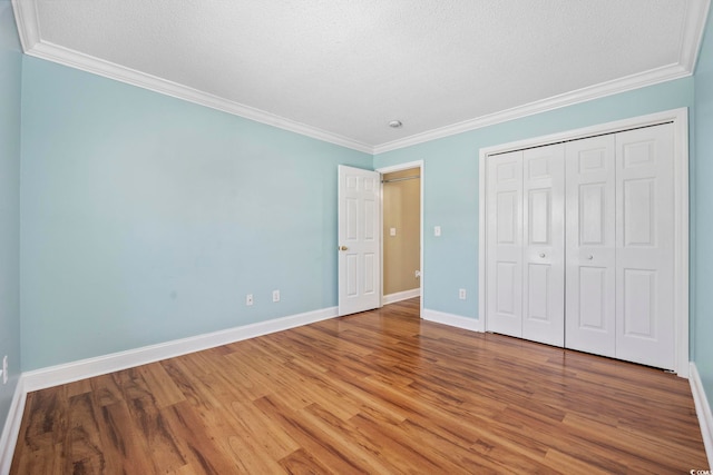 unfurnished bedroom with hardwood / wood-style floors, ornamental molding, and a closet