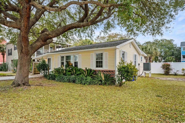 view of front of property with a front yard, brick siding, fence, and central AC