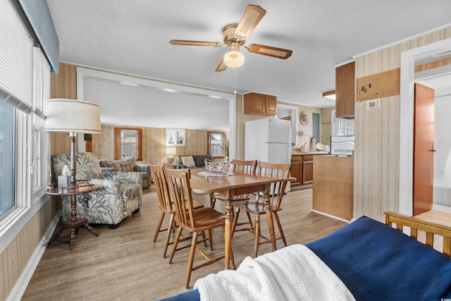 dining area with a textured ceiling, ceiling fan, light wood-type flooring, and wooden walls