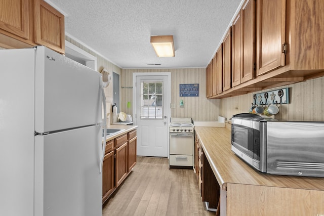 kitchen featuring brown cabinetry, white appliances, light wood-style floors, and a textured ceiling