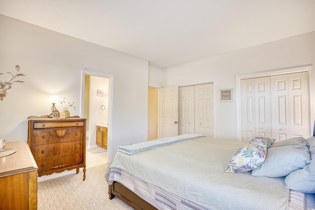 bedroom featuring light carpet, two closets, and connected bathroom