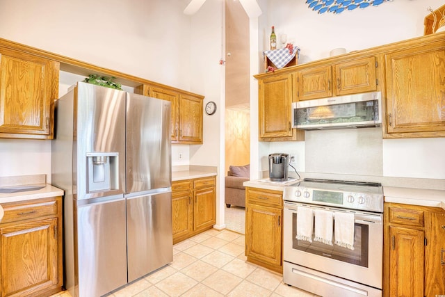 kitchen with stainless steel appliances, a towering ceiling, light tile patterned floors, and ceiling fan