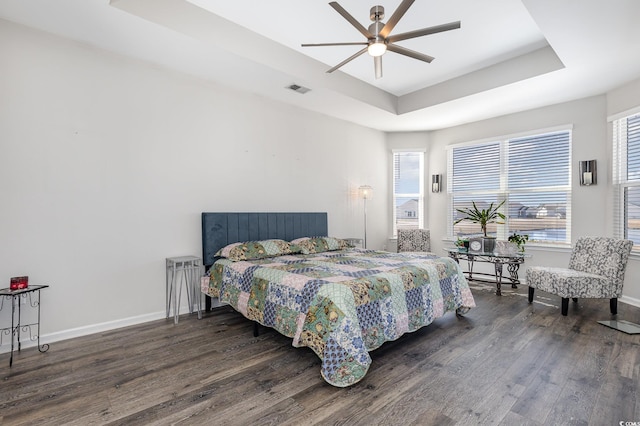 bedroom featuring multiple windows, dark wood-type flooring, ceiling fan, and a tray ceiling