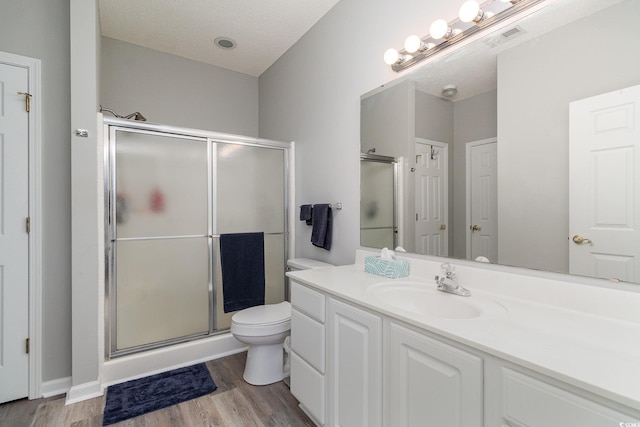 bathroom featuring toilet, wood finished floors, visible vents, vanity, and a shower stall