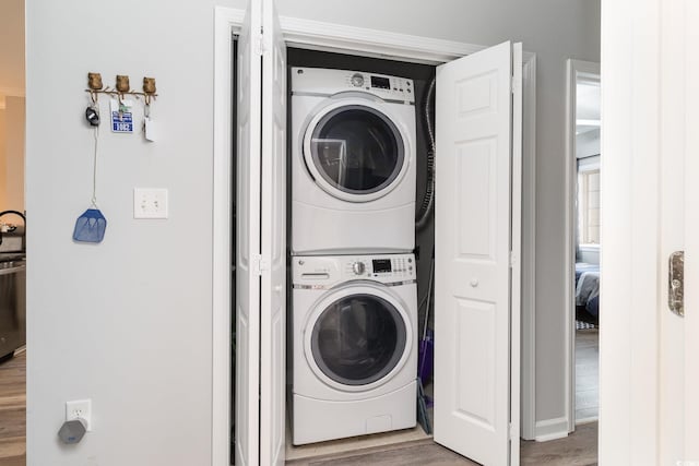 laundry room with laundry area, stacked washer and clothes dryer, and wood finished floors