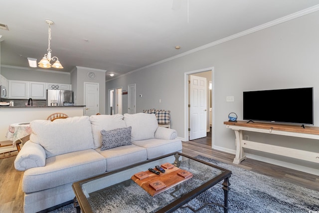 living room with a notable chandelier, wood finished floors, visible vents, baseboards, and ornamental molding