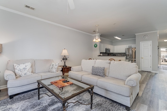 living room featuring ornamental molding, light wood-style flooring, visible vents, and baseboards