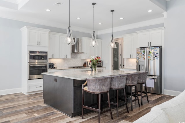 kitchen with hanging light fixtures, a kitchen breakfast bar, stainless steel appliances, white cabinets, and wall chimney exhaust hood