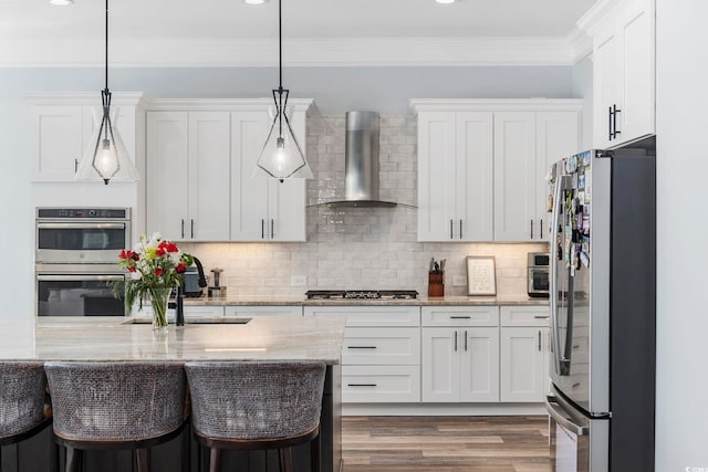 kitchen featuring white cabinetry, stainless steel appliances, decorative light fixtures, and wall chimney range hood