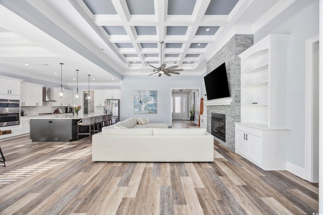 living room featuring coffered ceiling, a stone fireplace, light hardwood / wood-style floors, and beam ceiling