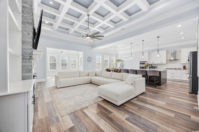 living room featuring coffered ceiling, crown molding, light wood-type flooring, ceiling fan, and beam ceiling