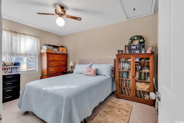 bedroom featuring attic access, light colored carpet, ceiling fan, and a textured ceiling