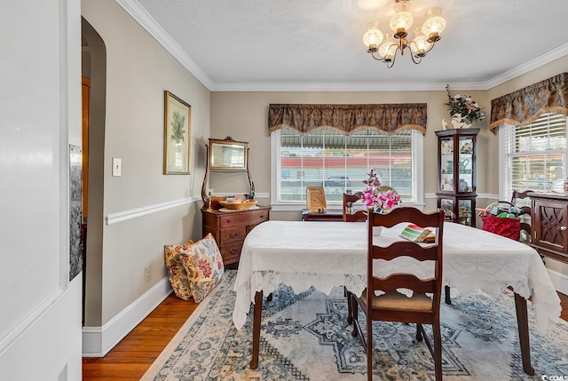 dining room featuring arched walkways, a healthy amount of sunlight, an inviting chandelier, and wood finished floors