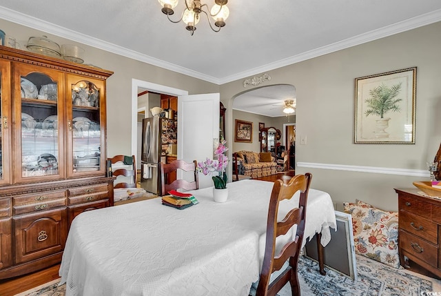 dining area featuring ornamental molding, arched walkways, and ceiling fan with notable chandelier