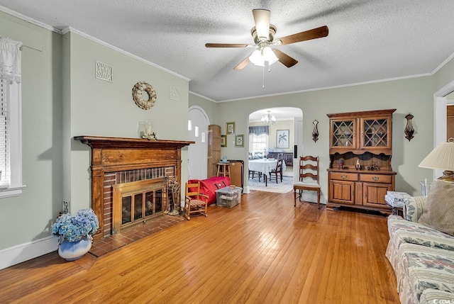 living room featuring arched walkways, wood finished floors, a textured ceiling, crown molding, and a fireplace