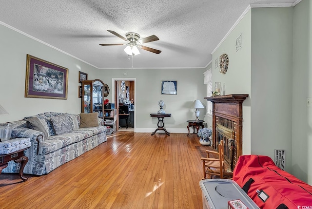 living area featuring a glass covered fireplace, ceiling fan, ornamental molding, wood finished floors, and a textured ceiling