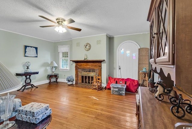 living area featuring ornamental molding, a fireplace, a textured ceiling, and wood finished floors