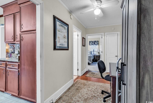 hall featuring a textured ceiling, light wood-type flooring, baseboards, and crown molding