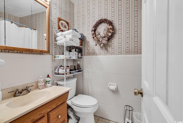 full bathroom featuring wallpapered walls, wainscoting, toilet, vanity, and tile walls