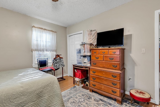 bedroom featuring light wood-type flooring, a textured ceiling, baseboards, and a closet