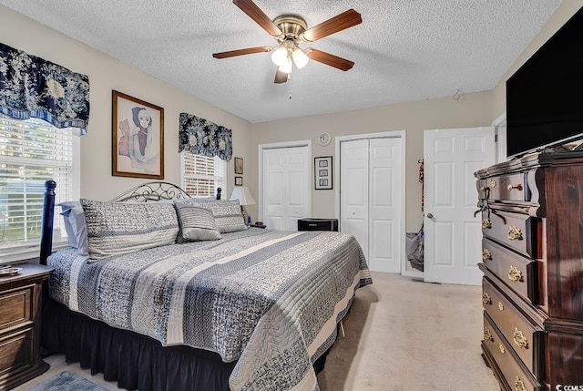 bedroom with multiple closets, light carpet, a textured ceiling, and a ceiling fan