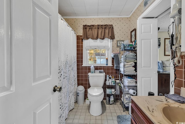 bathroom with wallpapered walls, toilet, tile patterned floors, vanity, and tile walls