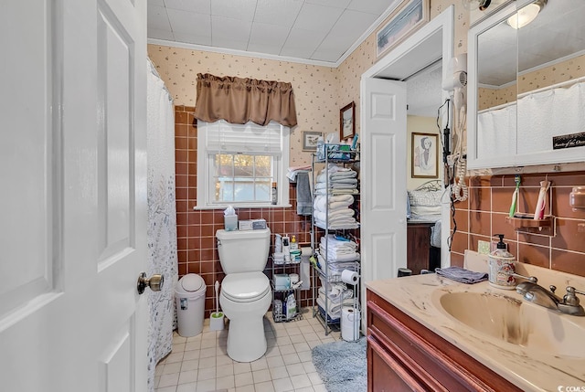 bathroom with wallpapered walls, toilet, tile patterned flooring, vanity, and tile walls