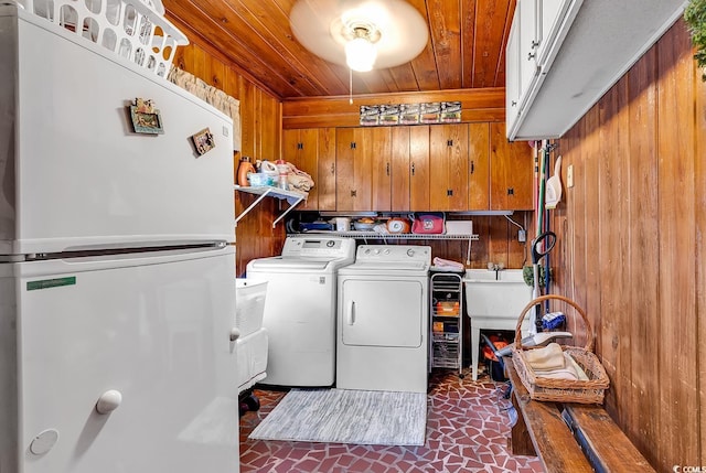 laundry room featuring wooden ceiling, wooden walls, a sink, cabinet space, and washer and clothes dryer