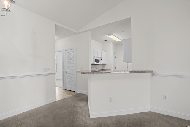 kitchen with kitchen peninsula, vaulted ceiling, light carpet, and white cabinets