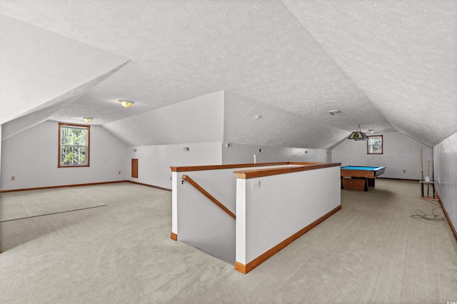 additional living space with billiards, light colored carpet, vaulted ceiling, and a textured ceiling