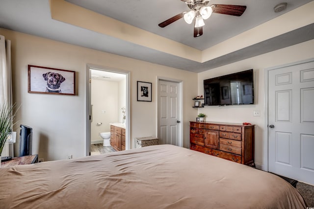 bedroom with hardwood / wood-style flooring, ceiling fan, ensuite bathroom, and a tray ceiling