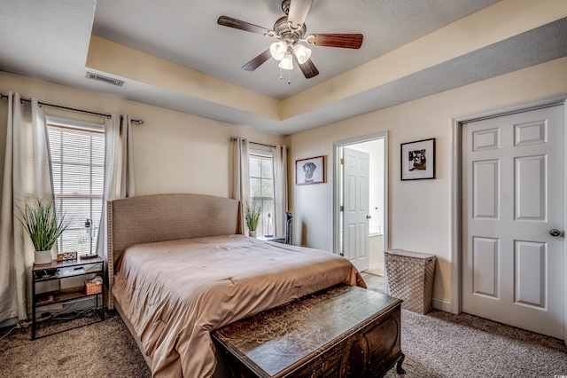 carpeted bedroom featuring ceiling fan, ensuite bathroom, and a raised ceiling