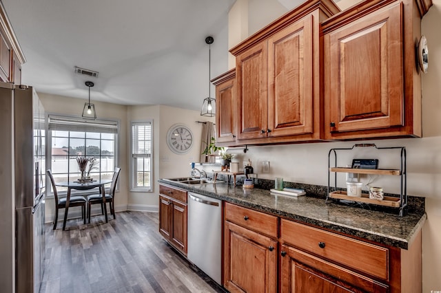 kitchen featuring sink, appliances with stainless steel finishes, dark hardwood / wood-style floors, decorative light fixtures, and dark stone counters