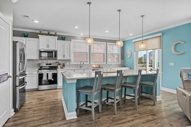 kitchen with appliances with stainless steel finishes, pendant lighting, white cabinetry, sink, and a center island