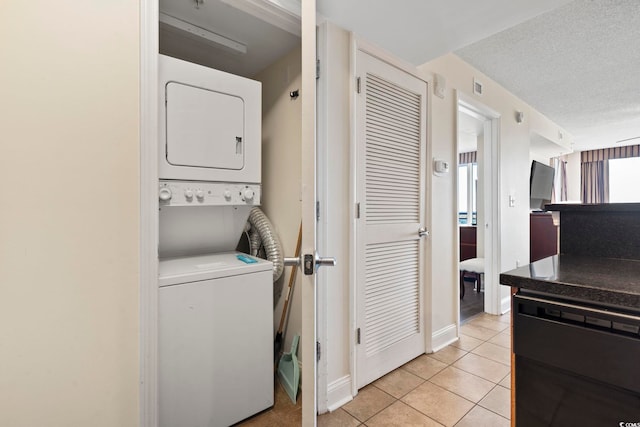 laundry area with light tile patterned floors, a textured ceiling, and stacked washing maching and dryer